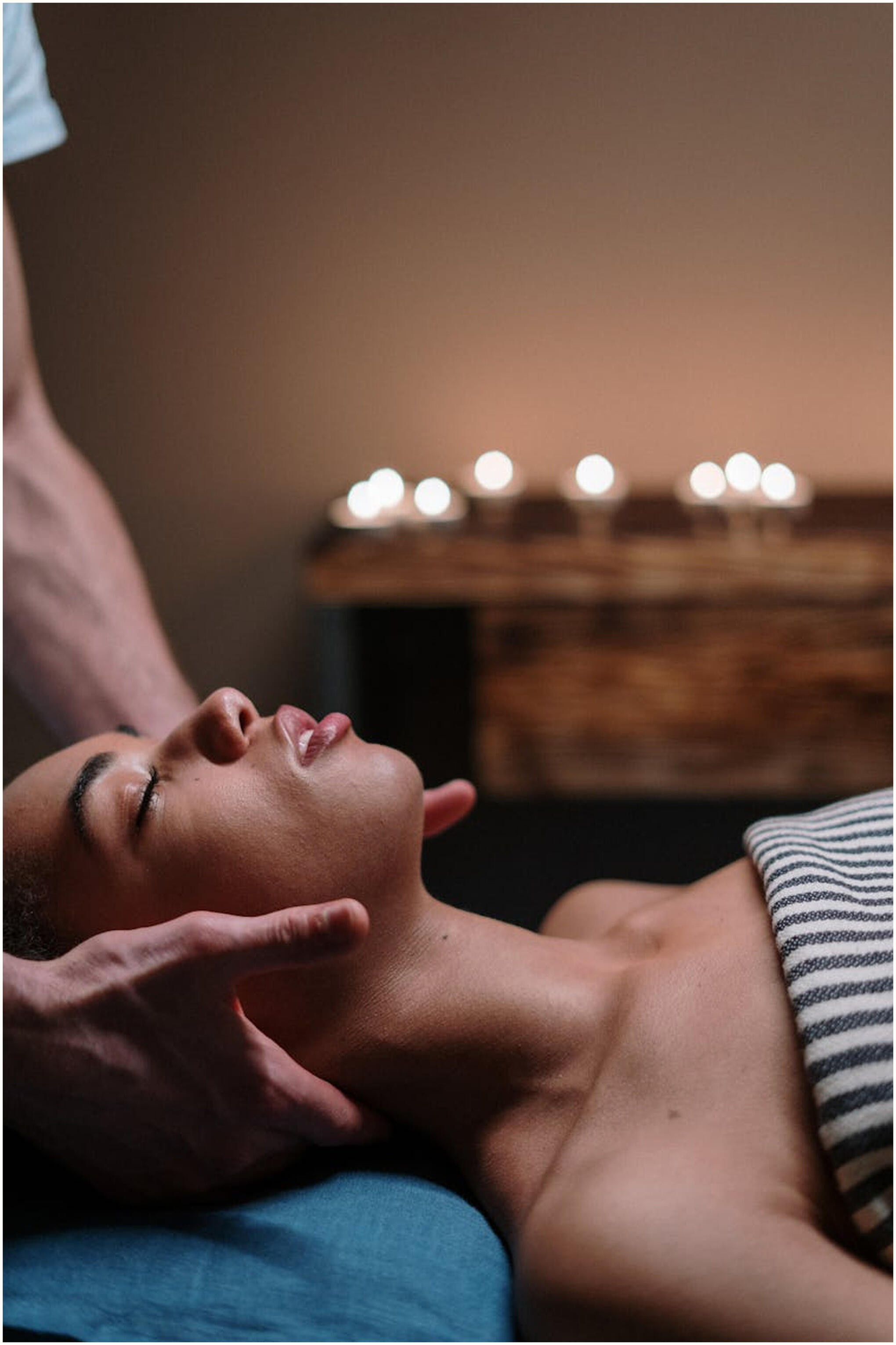 A woman chest up lying on a massage table with her eyes peacefully closed and strong hands of a masseuse gently cradling her head.