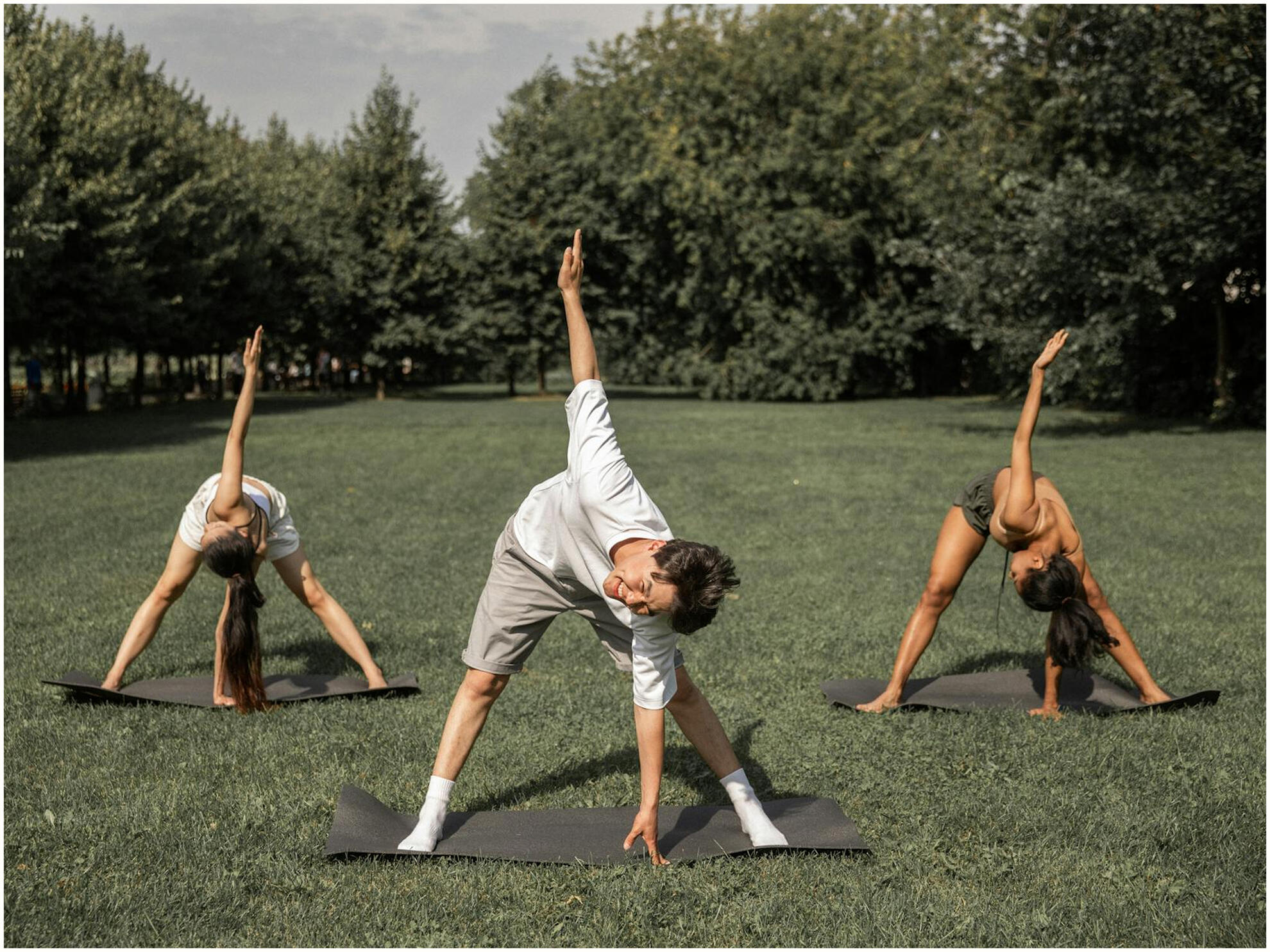 Two women and one man doing yoga outside on a lush green field.